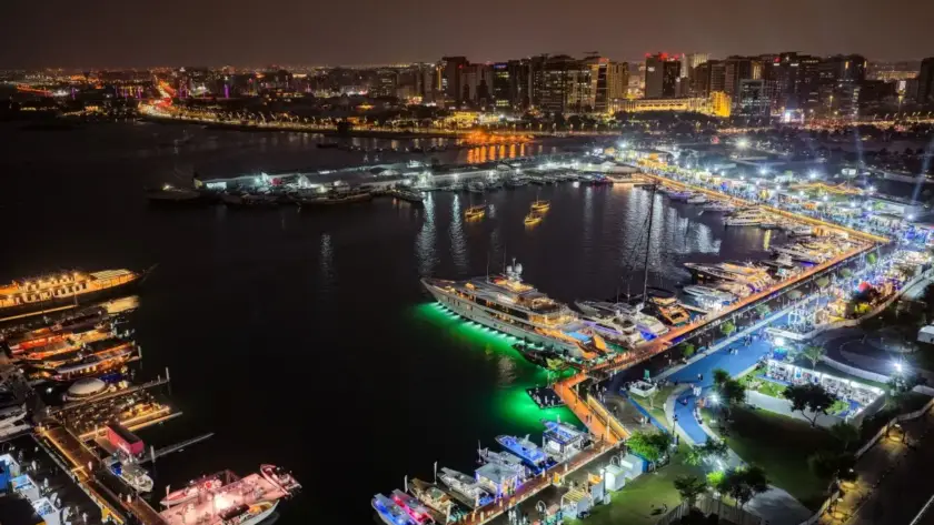 Nighttime aerial view of a luxury yacht exhibition and illuminated harbor marina.