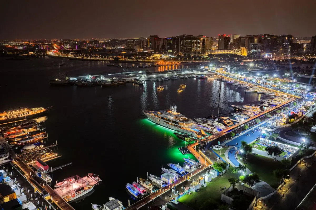 Nighttime aerial view of a luxury yacht exhibition and illuminated harbor marina.