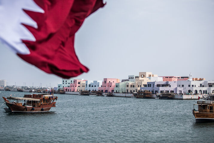 Qatar flag waving over traditional dhow boats at the Old Doha Port Mina District.