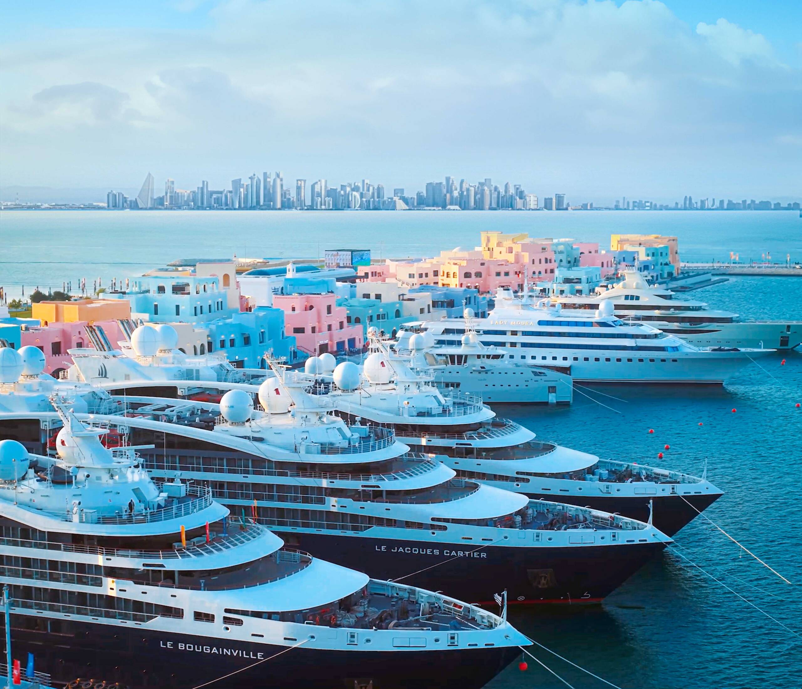 Superyachts docked at Old Doha Port with Doha's skyline across the waterfront.